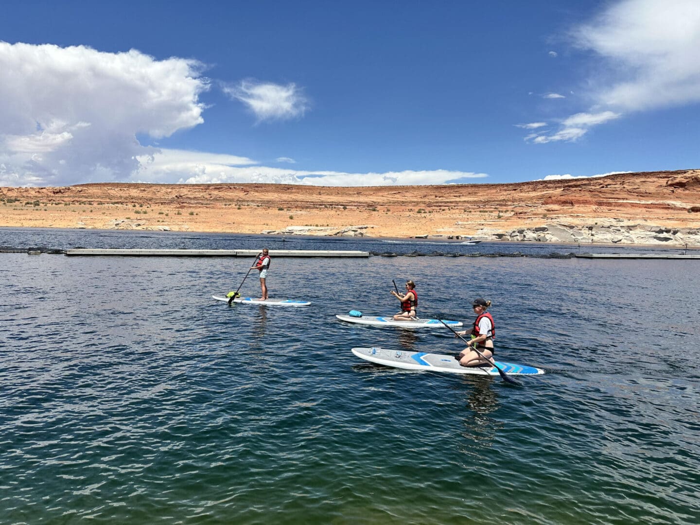 Three people paddle boarding on a lake near the shore.